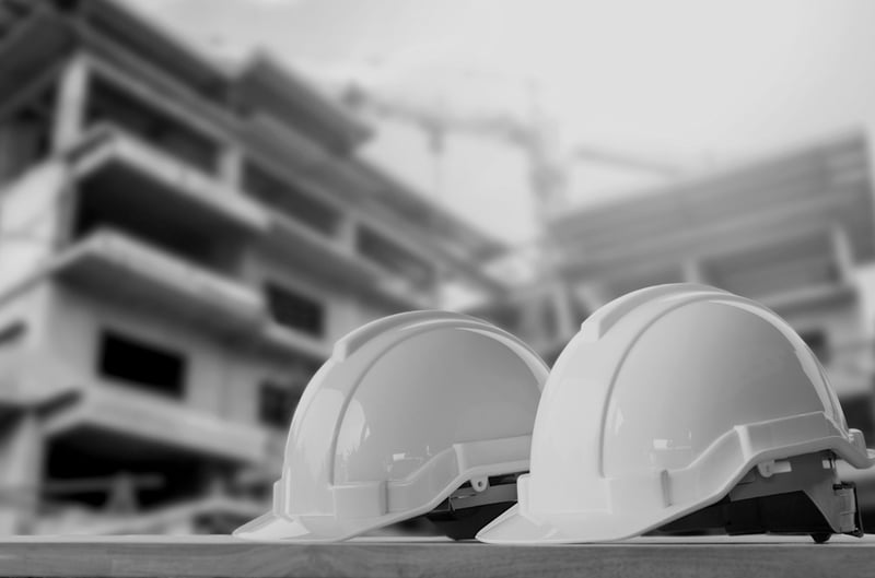 two construction hard hats outside near a worksite and building