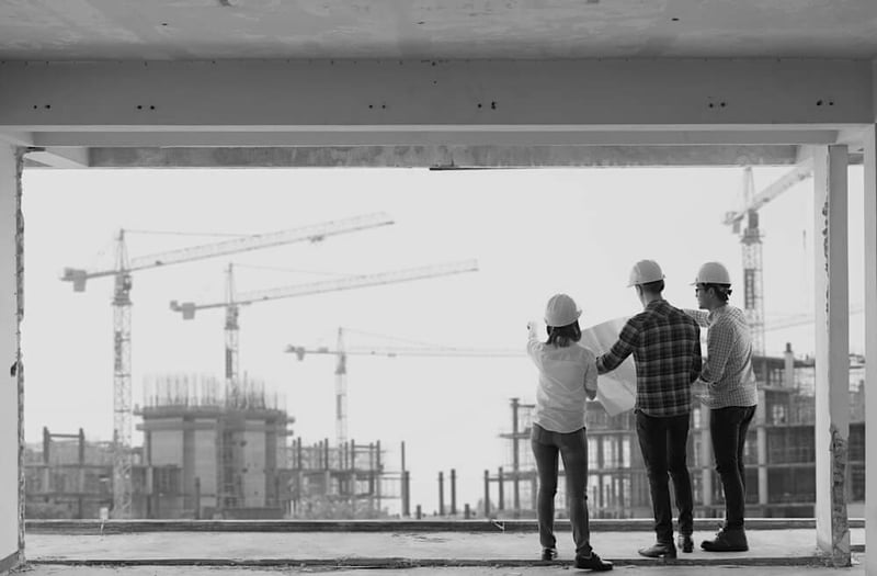 back view of three construction workers in building looking out large window at project site