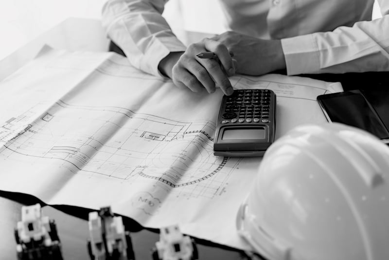 business man using calculator on construction job plans at desk