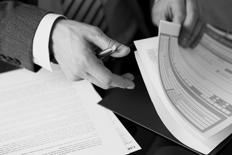 businessman hand with pen reviewing documents in a large stack of papers