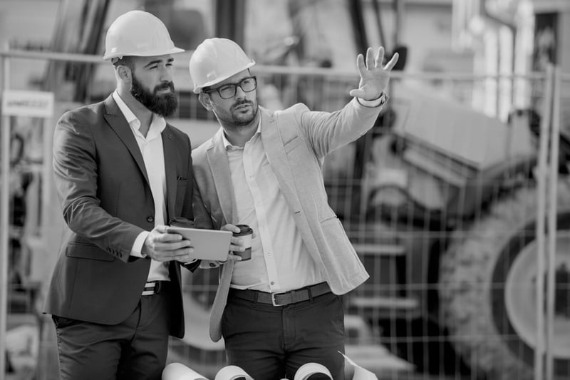 male construction worker with hardhat and coffee showing jobsite to his partner