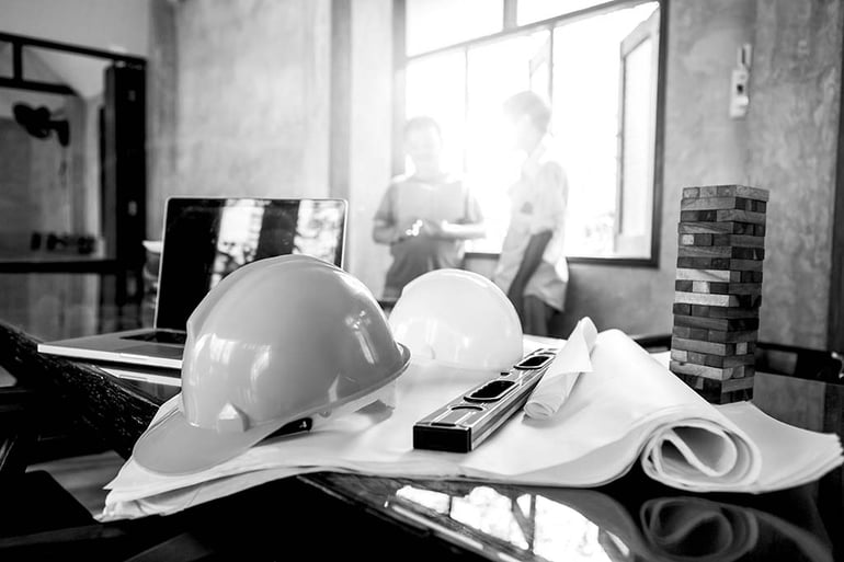 construction hardhats on desk with laptop, wooden blocks, and construction documents