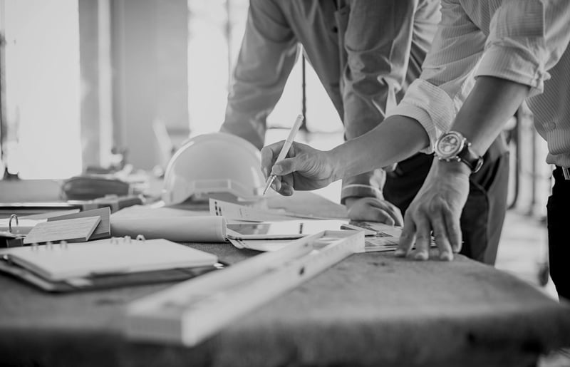 contractors at desk assessing construction plans with pencil, ruler, and hardhat