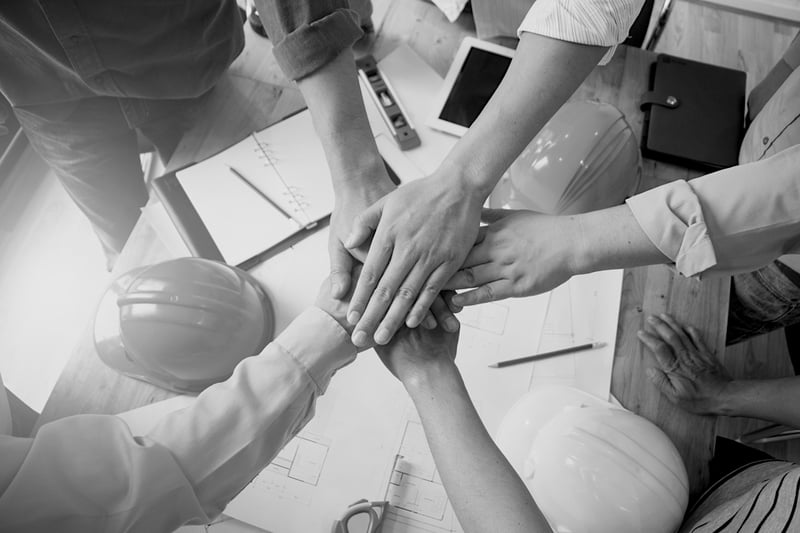 group of coworkers put their hands together over a cluttered work desk