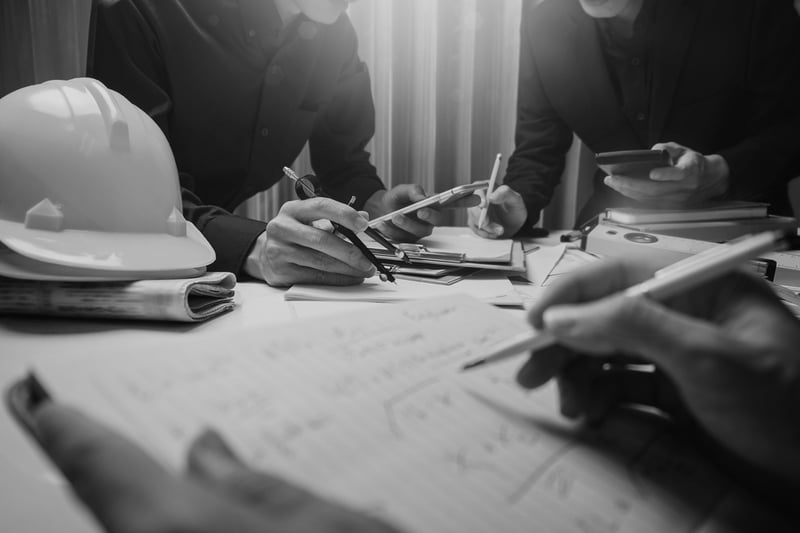 group of contractors writing documents at desk with construction hardhat