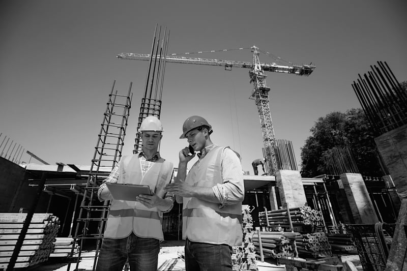 two construction workers with hardhats discussing plans in front of jobsite