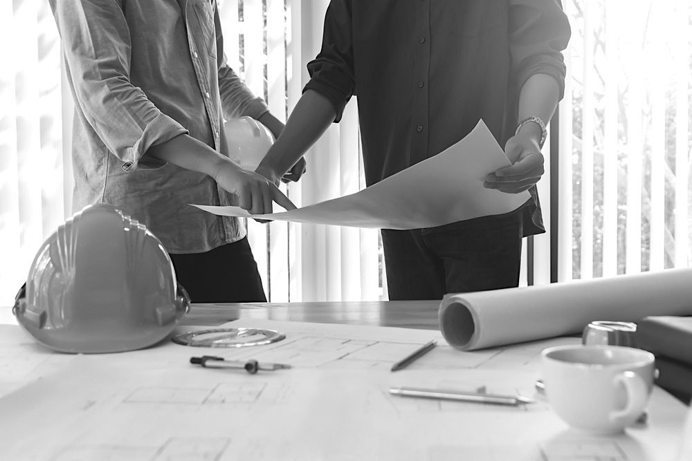 two contractors reviewing construction plans at desk with with hardhat and pencils