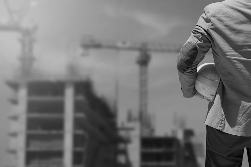 construction worker with a hardhat in his hand standing in front of jobsite 