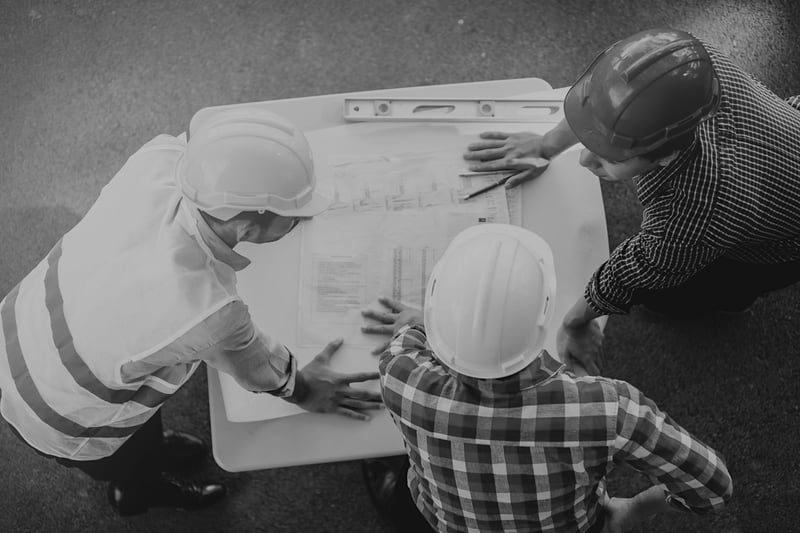 three construction workers with hardhats reviewing worksite documents at a table