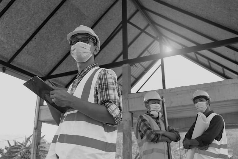 team of three construction engineers wearing masks and hardhats at a construction site under a roof