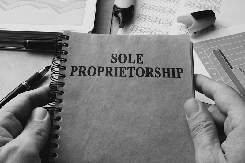 person in front of cluttered desk holding notebook with sole proprietorship