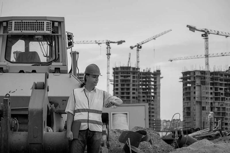 male construction worker standing by a tractor at worksite and looking at watch