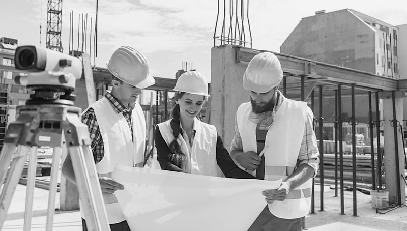 female construction worker showing jobsite plans to two male workers at construction site 