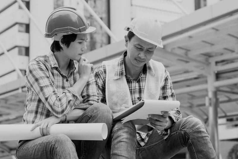 female and male Asian-American construction workers with hardhats reviewing work plans at construction site