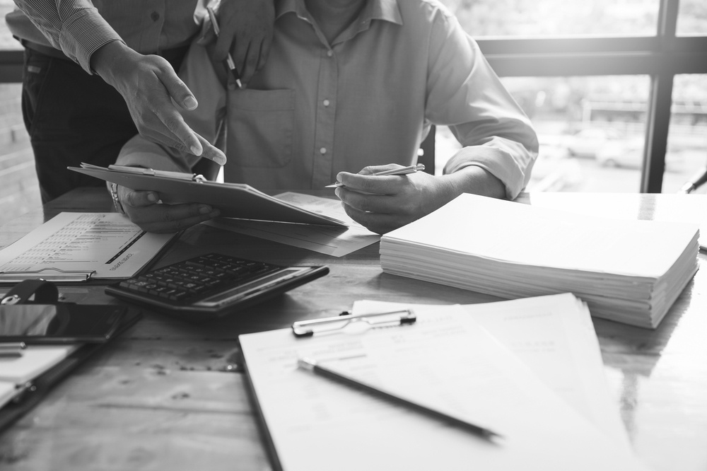 two businessmen reviewing insurance documents at desk with calculator and stacks of papers