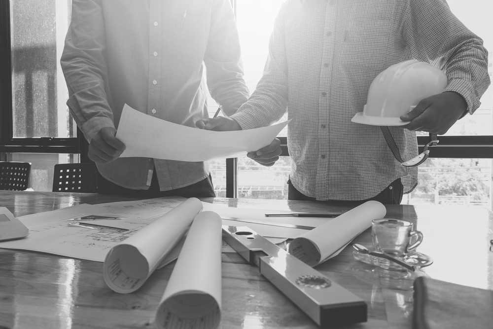 two construction workers reviewing job site plans in front of table with hardhat and drafting equipment