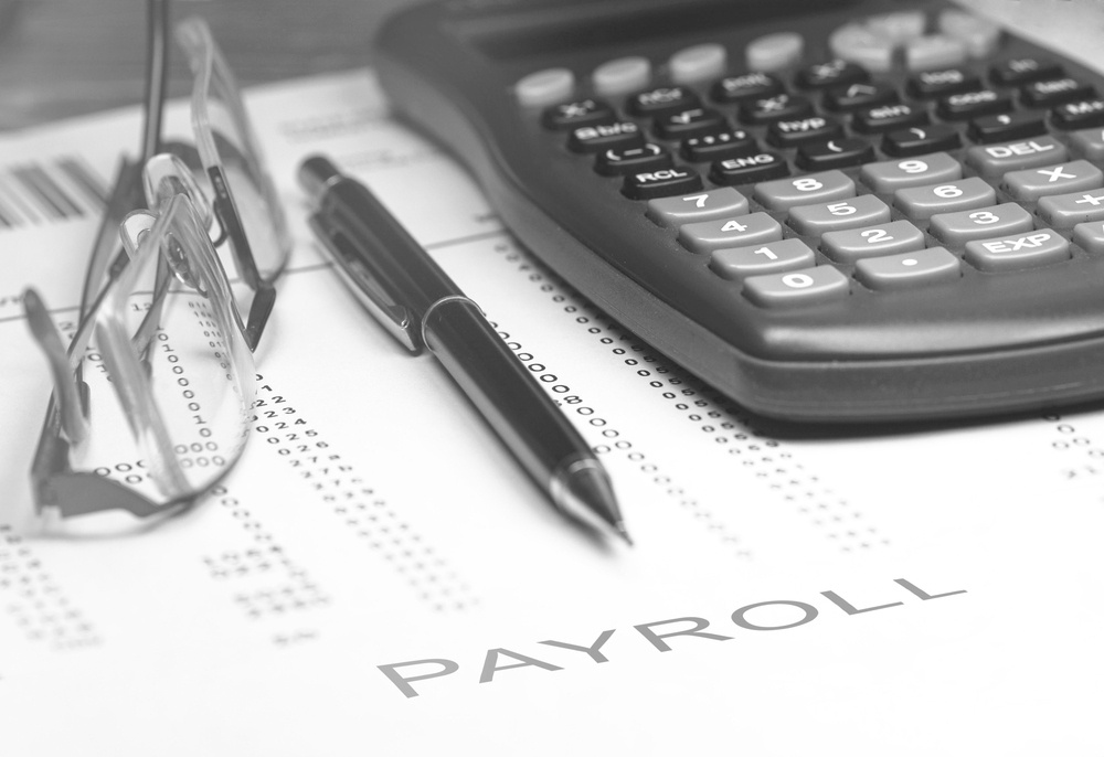 payroll document on desk with glasses, pen, and calculator