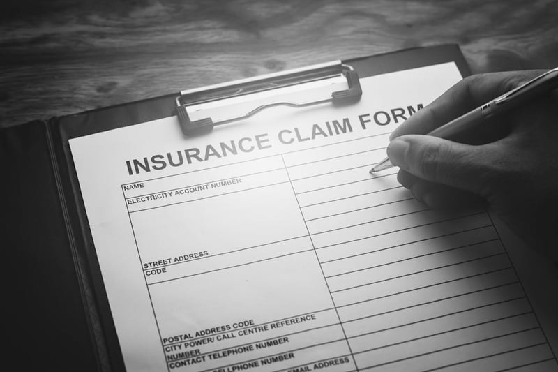 hand signing insurance claim form with pen on wooden desk
