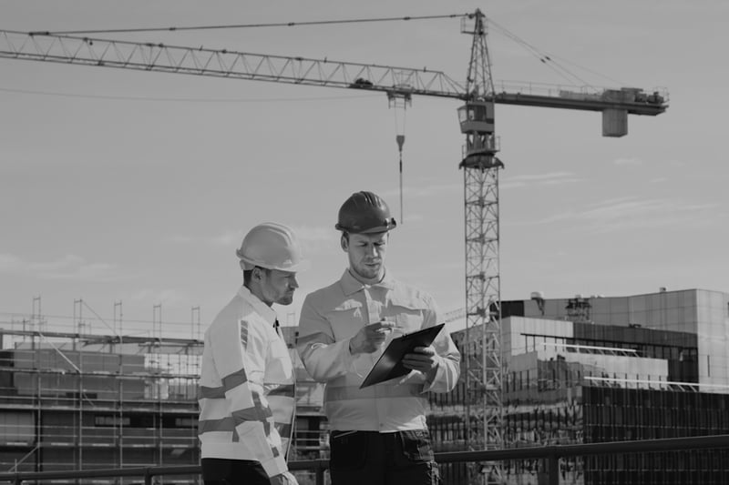 two construction workers reviewing documents outside at worksite near large crane