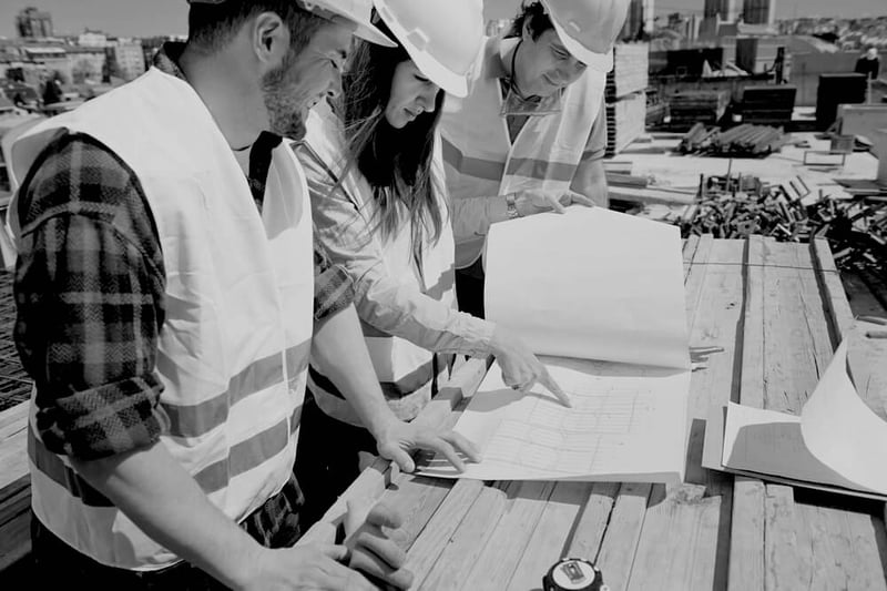 three construction workers with hard hats and uniforms reviewing documents outside of worksite