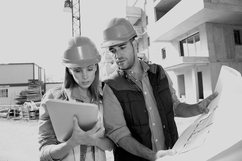female contractor holding notepad with male contractor holding jobsite sketch outside