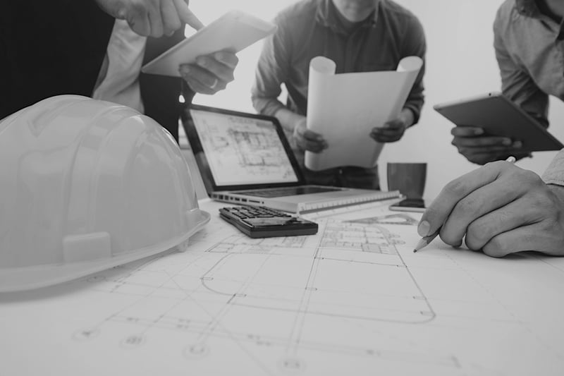 team of contractors reviewing construction plans at desk with hard hat, laptop, and calculator