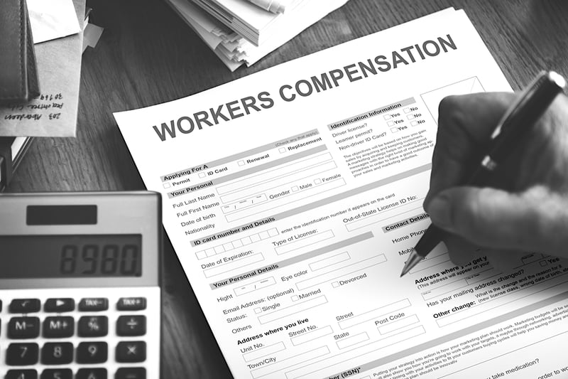 person signing a workers compensation form on a desk with a calculator