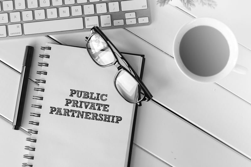 notebook with public private partnership on a desk with coffee cup, keyboard, and glasses