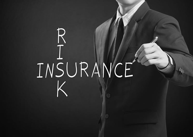 business man writes risk insurance with a pen over black background