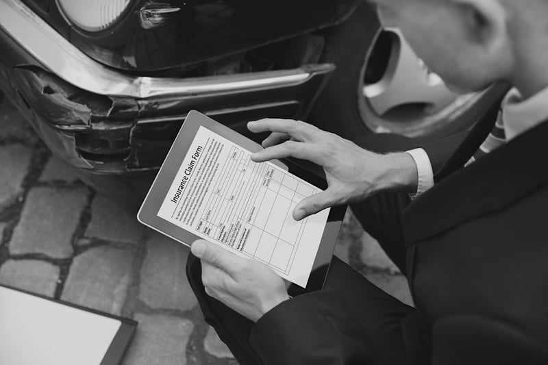 business man holding insurance claim form paper in front of damaged vehicle 