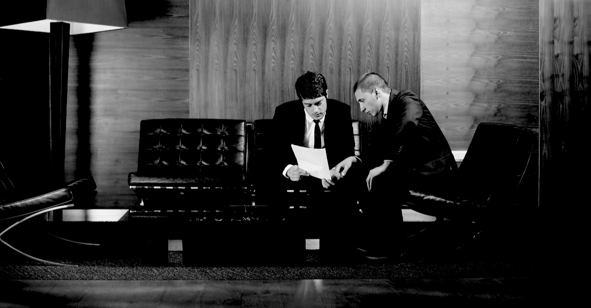 two businessmen sitting on couch and reviewing insurance papers