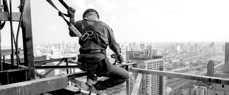 Construction worker on very tall scaffolding with a hard hat and safety harness