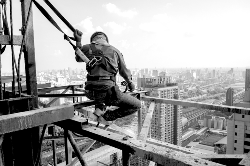 Construction worker wearing a safety harness while working up in the air on a skyscraper.
