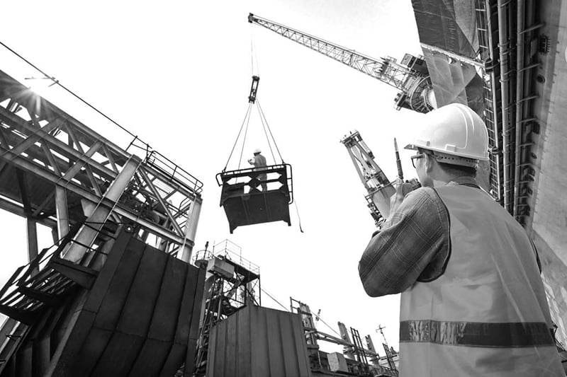 Construction worker lifting crane and using walkie talkie.