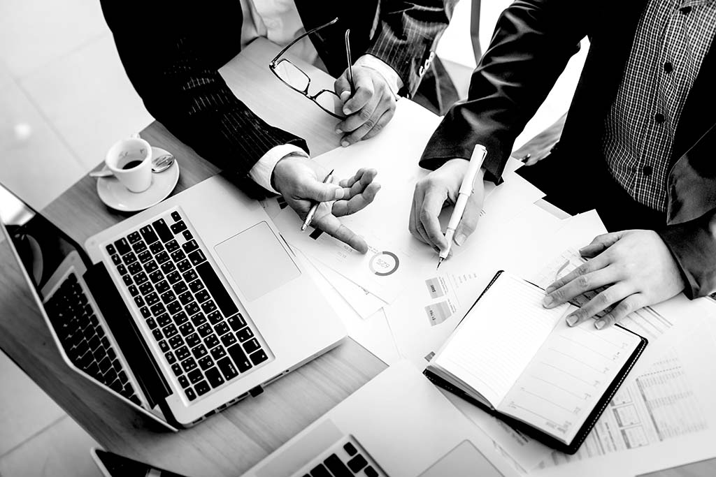 two businessmen pointing at paper documents on table with laptop and coffee cup