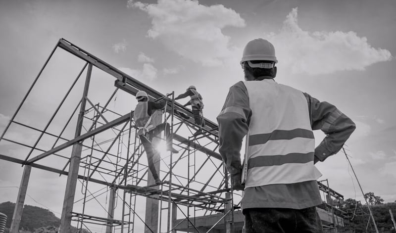 male construction worker in uniform watching team of two other workers building a high steel platform outside