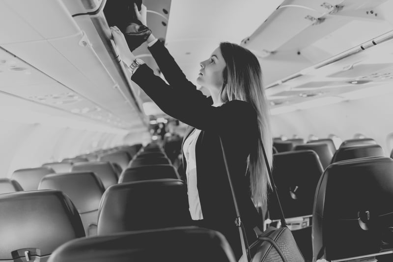 university woman packing luggage in overhead bin on airplane