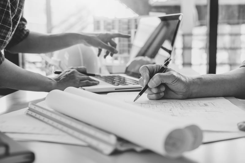 contractor writing document while other worker points at computer screen