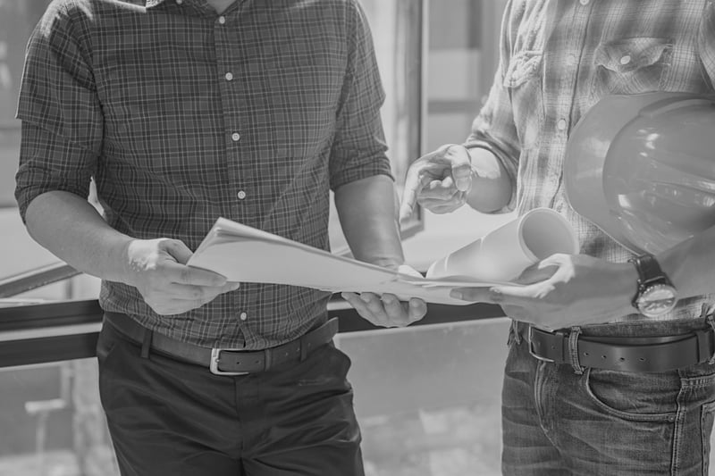 two construction workers visible from neck down reviewing plans