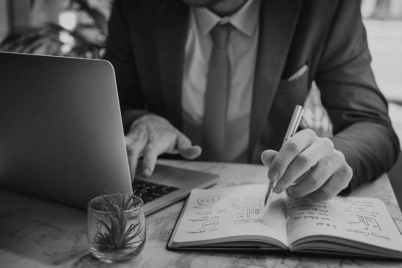 businessman with laptop and open notebook taking notes