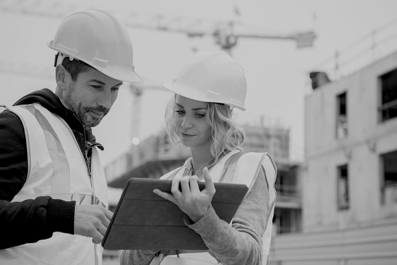 construction male and female workers reviewing documents on tablet at construction site