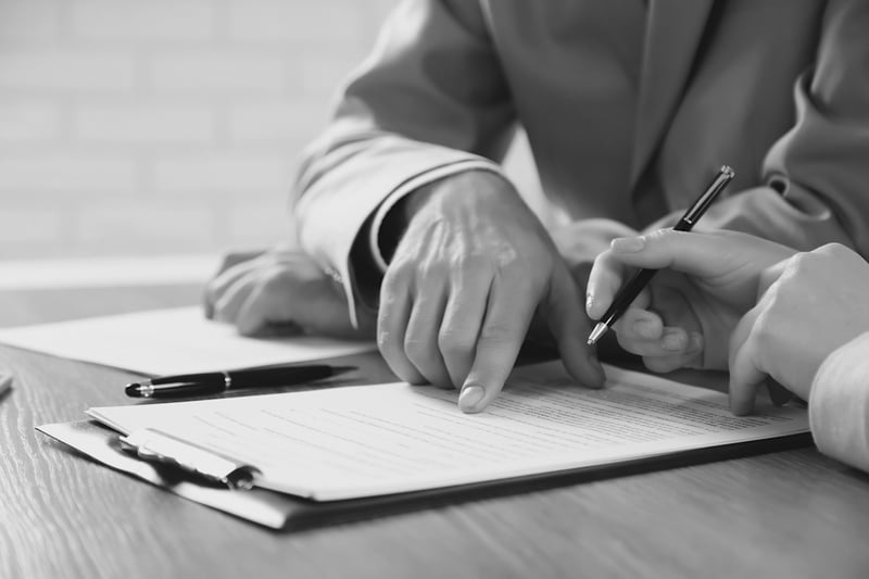 two colleagues signing paper form on a clipboard