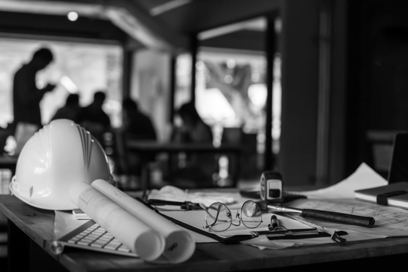 table with construction equipment including hardhat, hammer, glasses, and paper plans 