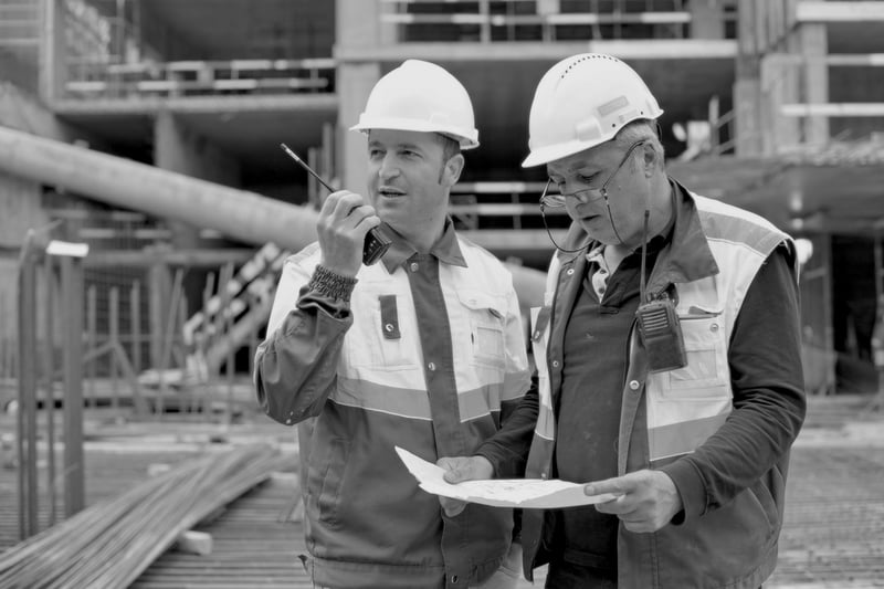 two senior construction workers with hardhats reviewing documents at construction site 