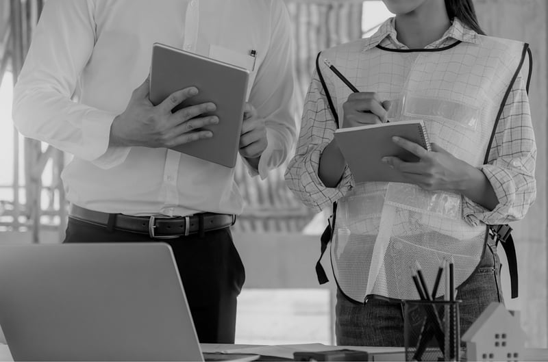 male and female contractors reviewing notebooks at desk with pencils and laptop