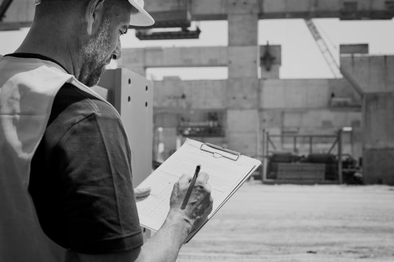 construction worker with hardhat writing on clipboard at construction worksite