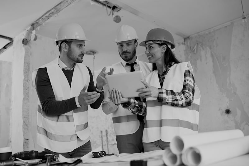 three construction workers with hard hats and uniforms reviewing plans together in work building