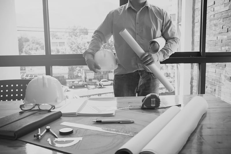 construction worker holding hardhat and construction plans in front of cluttered desk