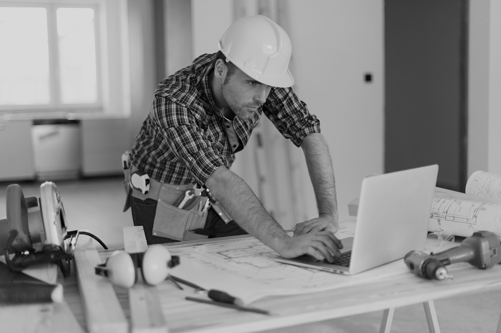 construction worker with hardhat using laptop on desk with construction tools