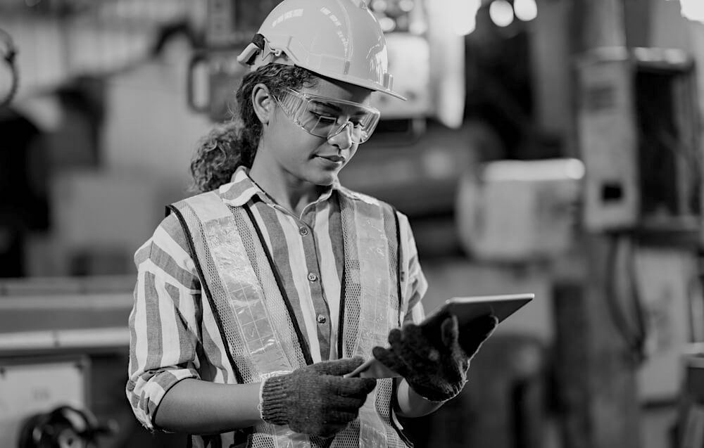 female construction worker with hardhat and goggles reviewing work plans on a tablet in a factory